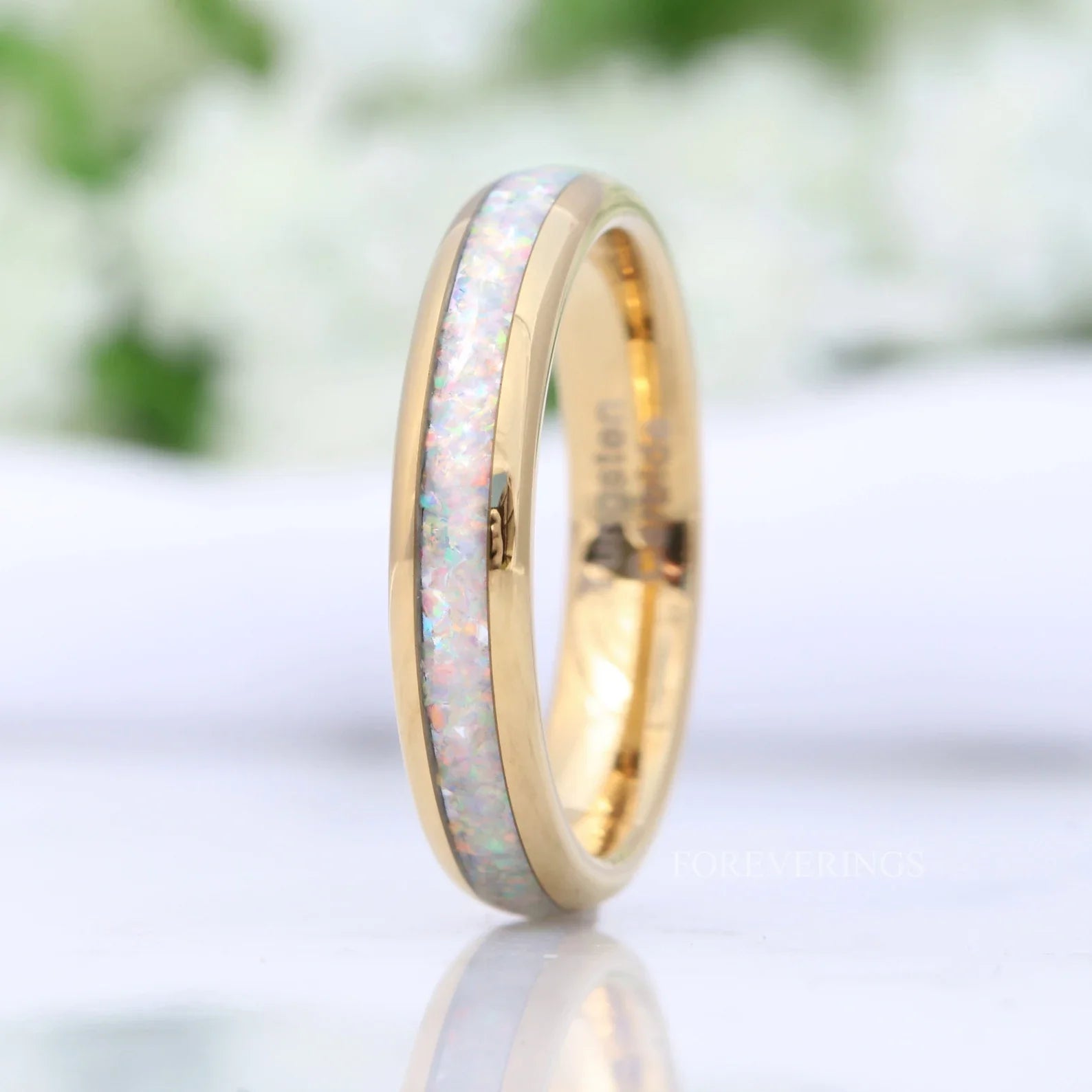 Close-up of a tungsten ring on a marble surface, showcasing white opal inlay and polished finish