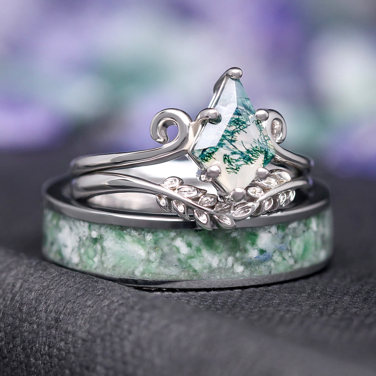 Moss agate engagement ring set standing behind a wide silver tungsten band with moss agate inlay