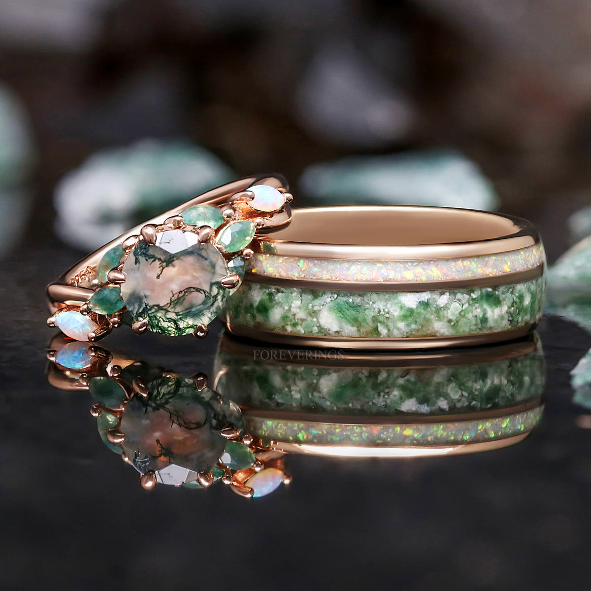 Moss agate engagement ring lying beside the wider rose gold tungsten ring with moss agate and opal inlay