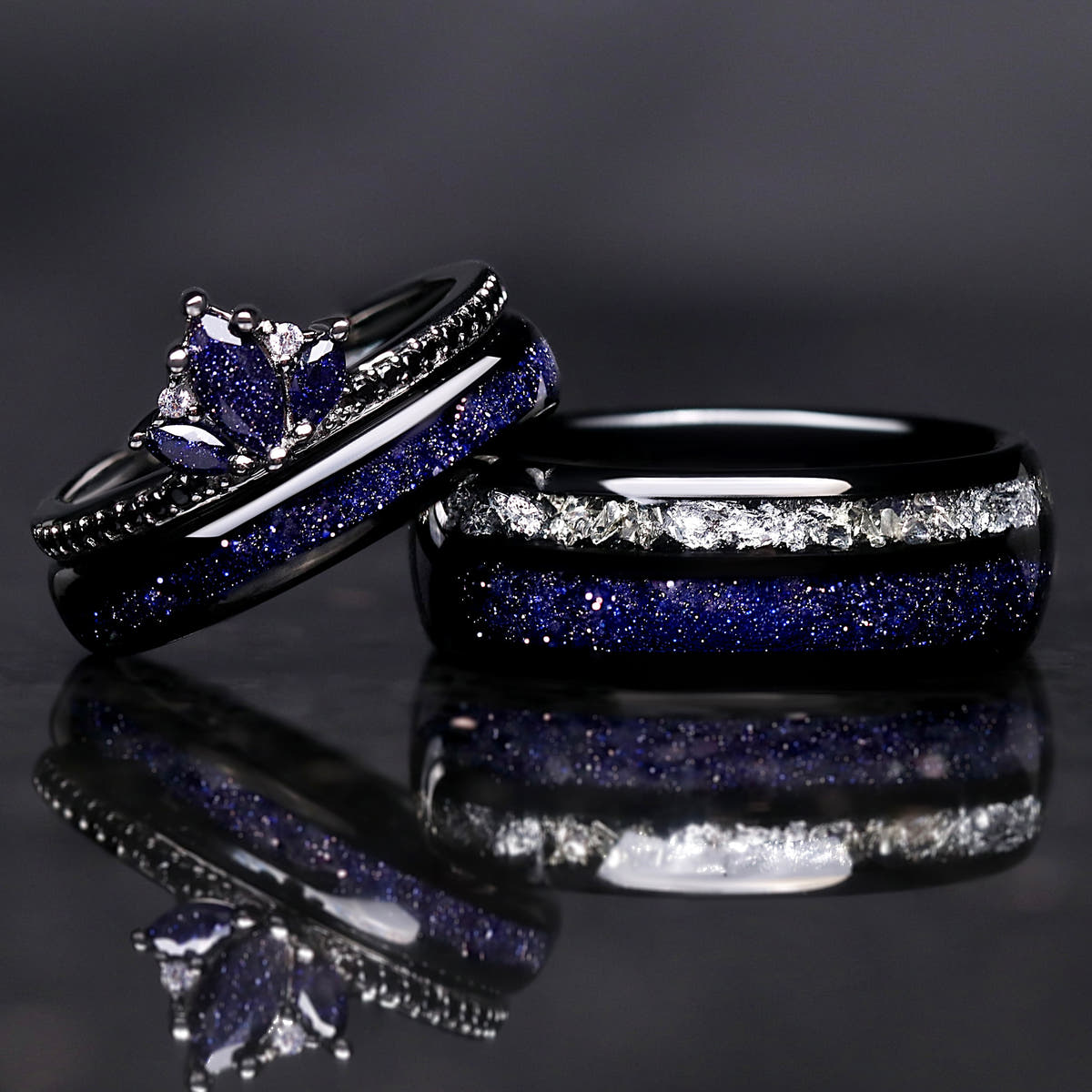 Two black rings with blue and white gemstones on a reflective surface.