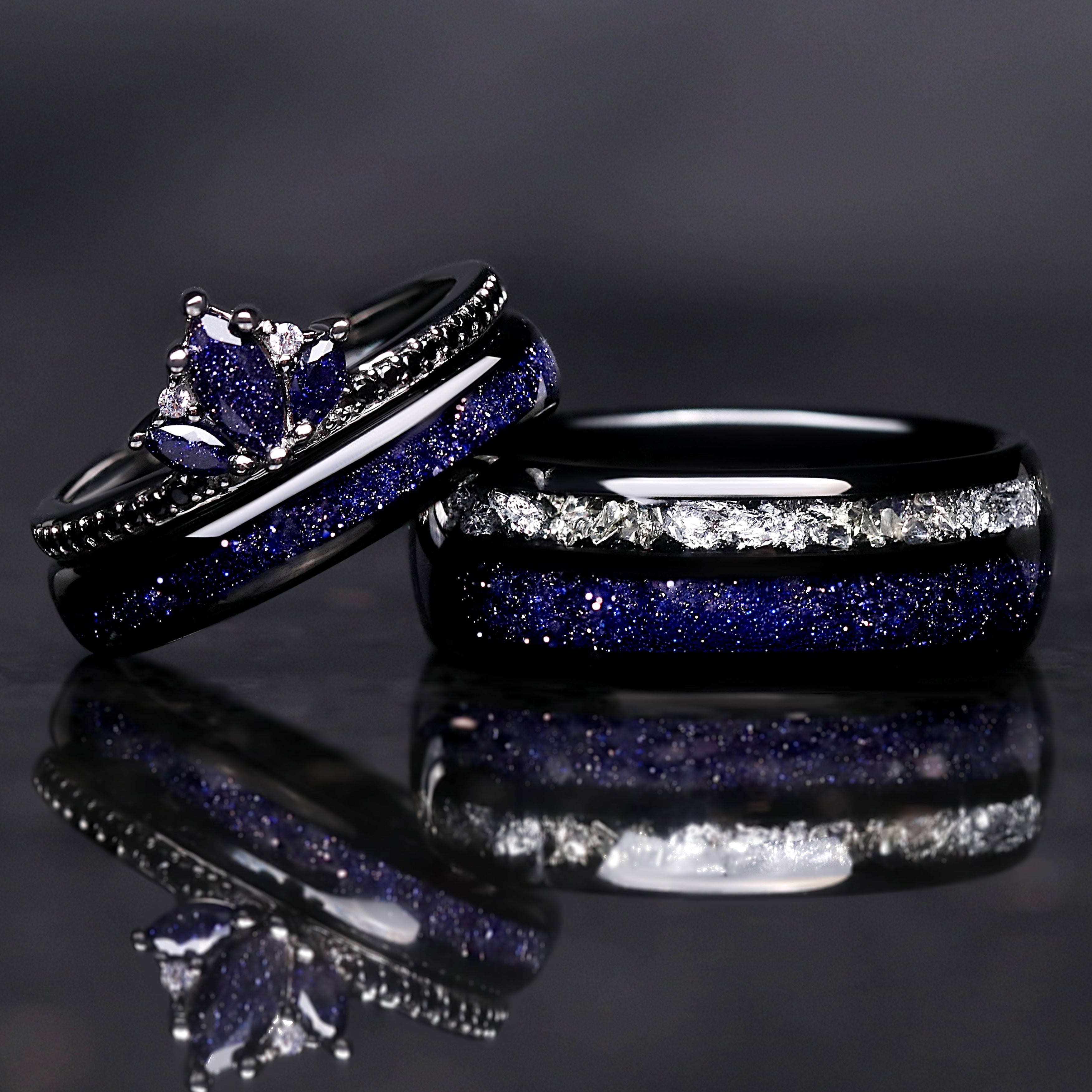 Two black rings with blue and white gemstones on a reflective surface.