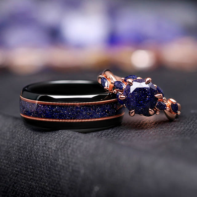 Black tungsten guitar string band beside a rose gold engagement ring with a dark blue center stone
