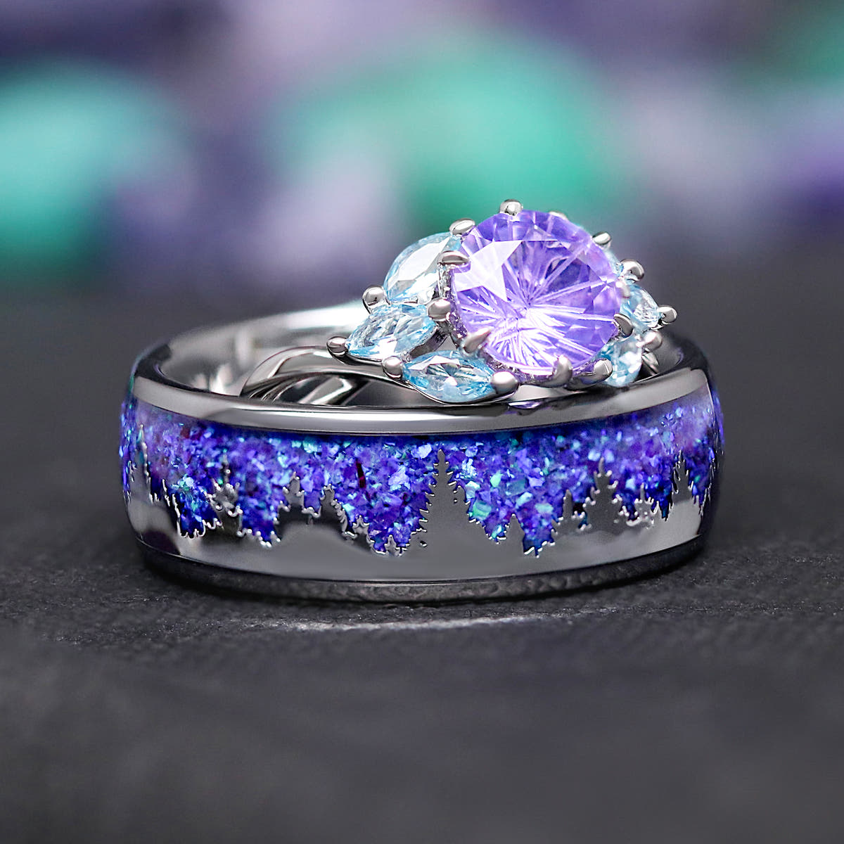 Amethyst ring resting on a wider silver band with a purple mountain landscape inlay