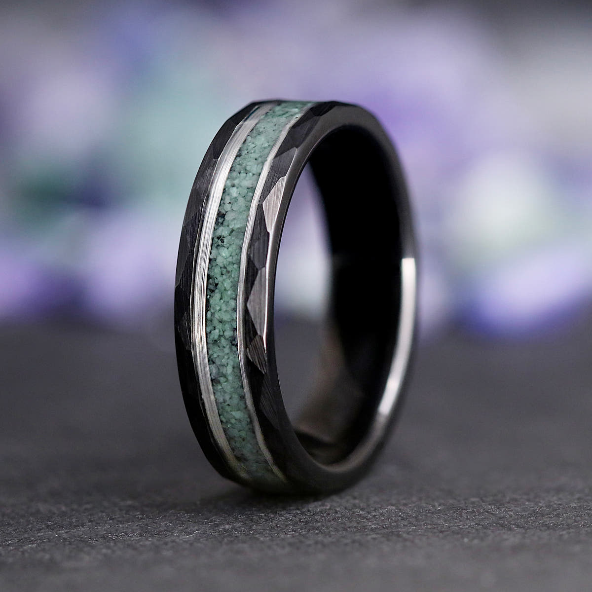 Men's 6mm black tungsten ring with crushed green moss agate inlay, standing on edge