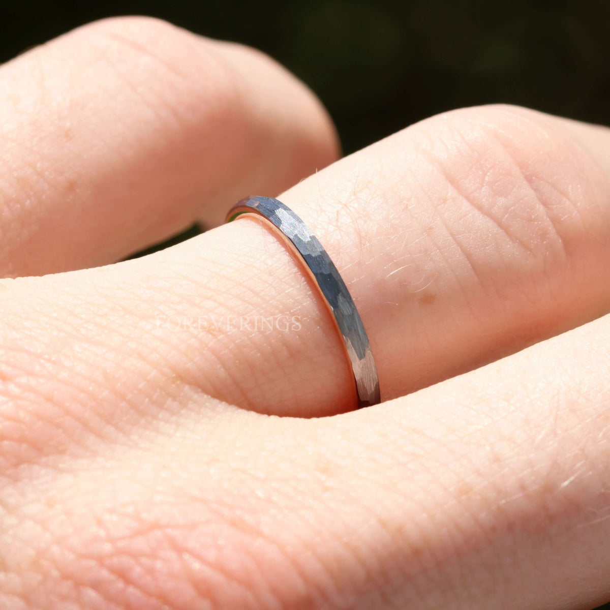 Close-up of a hammered silver tungsten band with rose gold interior worn on a finger