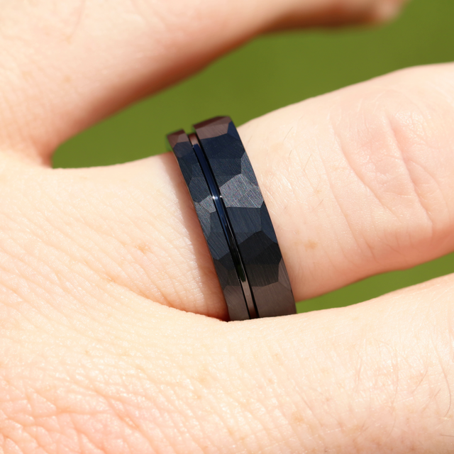 Hammered black tungsten band with an offset groove, worn on a finger