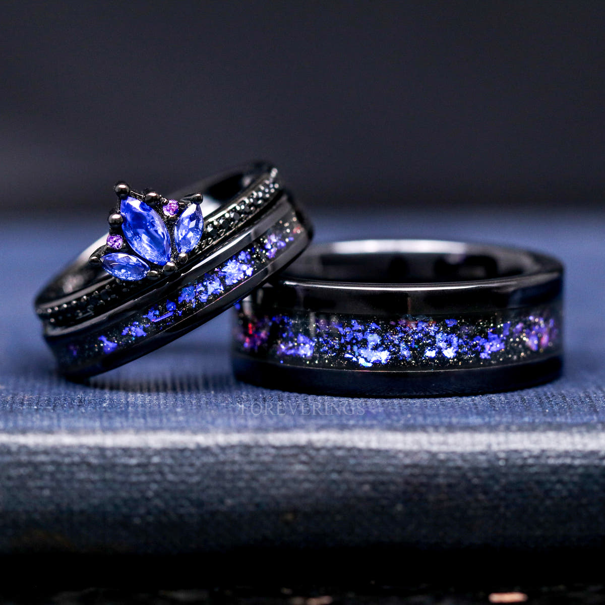 Blue sapphire lotus ring leaning on black tungsten bands with nebula inlay