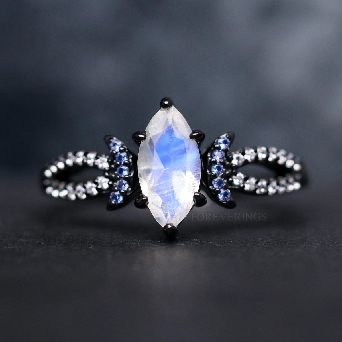 Women's black sterling silver marquise moonstone ring with blue sapphire crescent accents, close crop