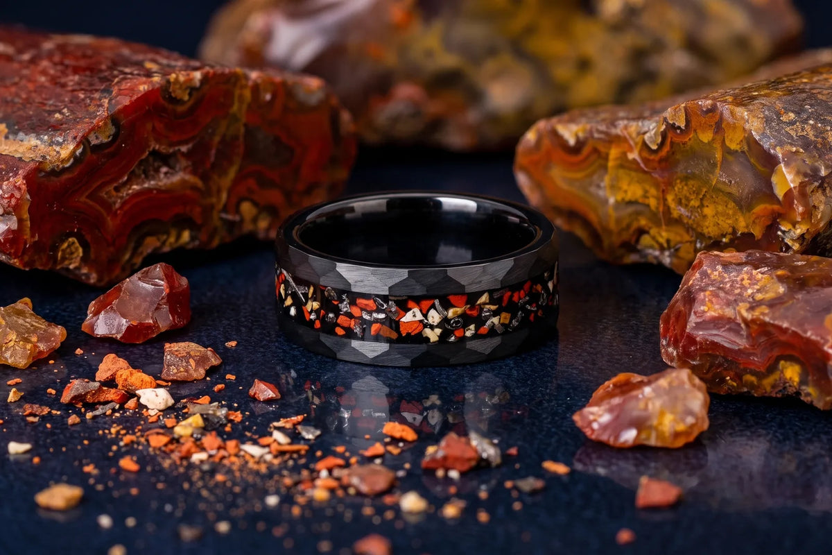Hammered black tungsten dinosaur bone ring beside agatized fossil pieces
