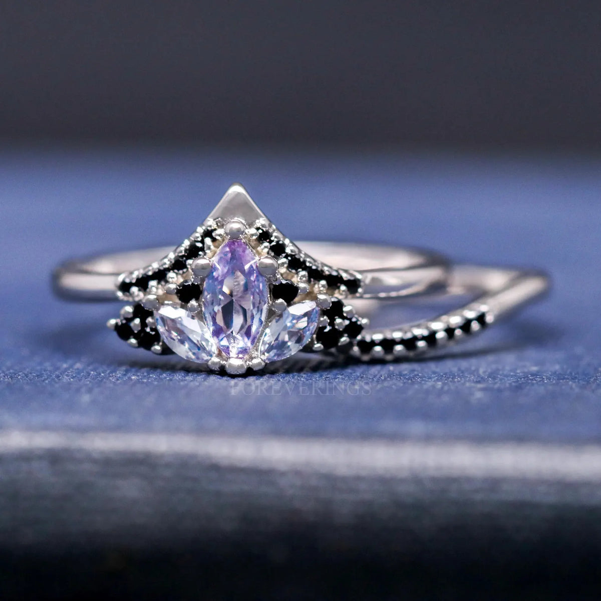 Alexandrite lotus engagement ring with its curved black accent band set beside it
