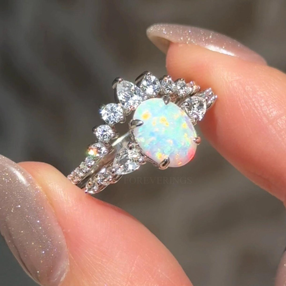 Oval white fire opal engagement ring and curved band held between fingertips