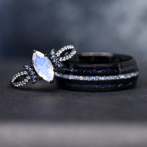 Matching black couples rings: marquise moonstone ring leaning on an 8mm tungsten ring with blue sandstone stripes