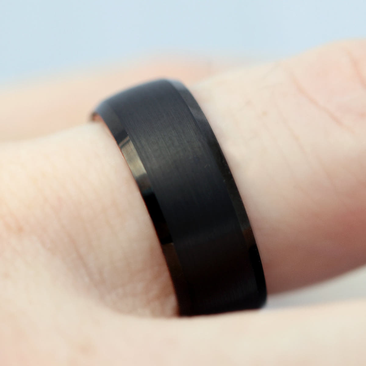 Men's brushed black tungsten band with beveled edges worn on a finger