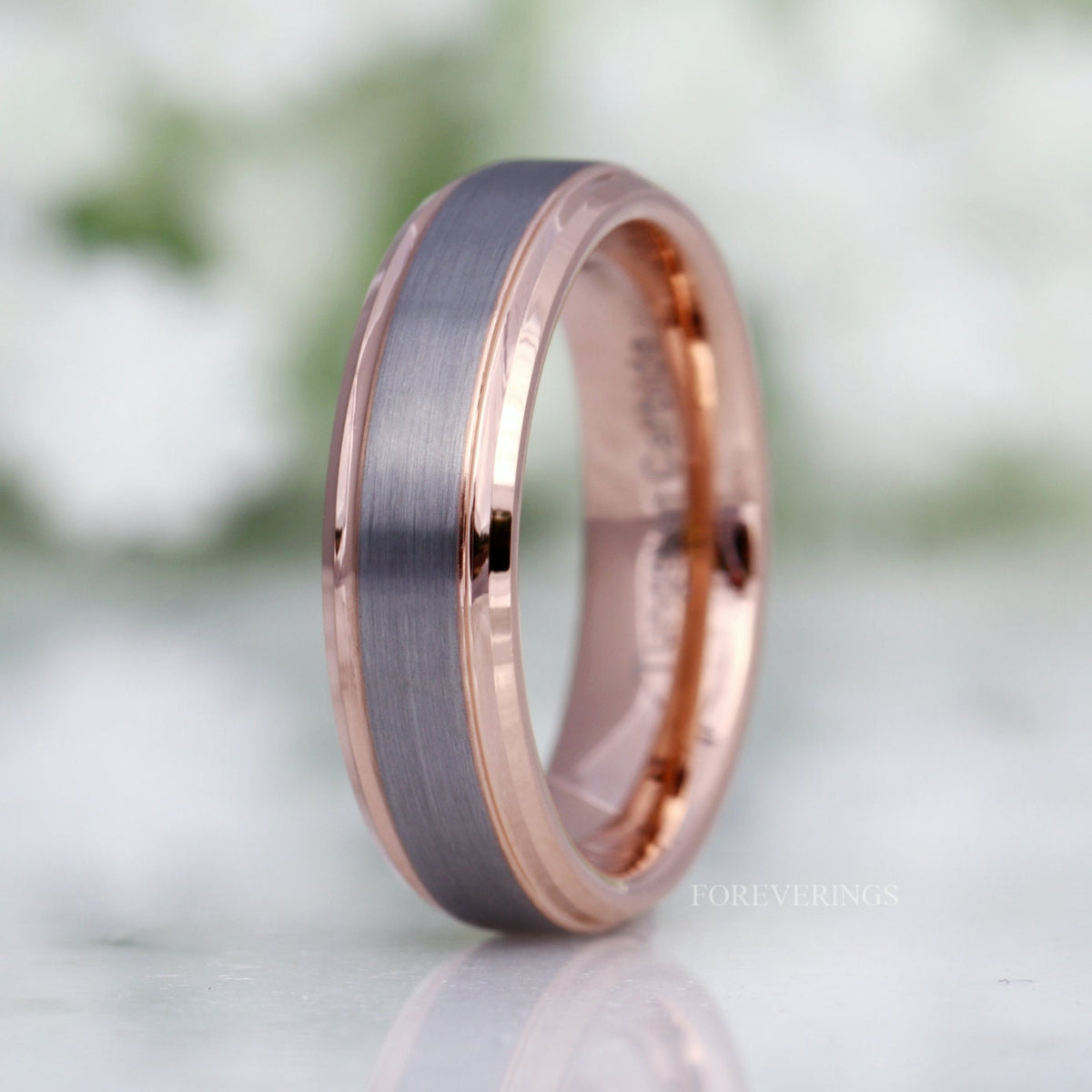 Men's matte silver tungsten wedding band with rose gold beveled edges, standing at an angle