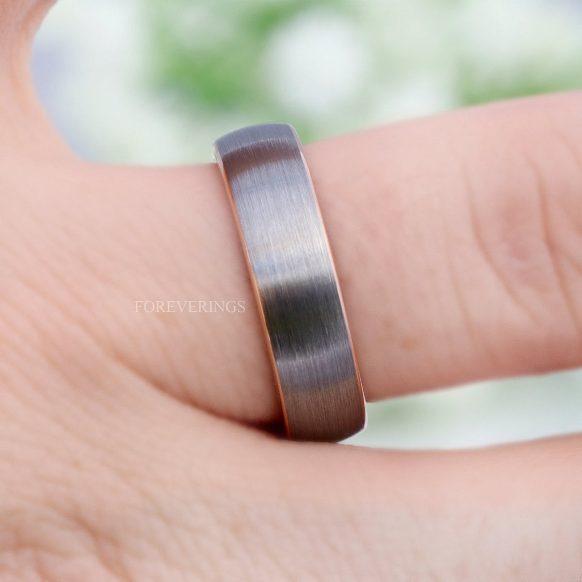 Men's brushed silver tungsten band with rose gold inside worn on a finger