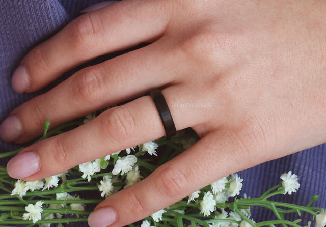 Matte black two-tone tungsten ring worn on a woman's hand, wider view