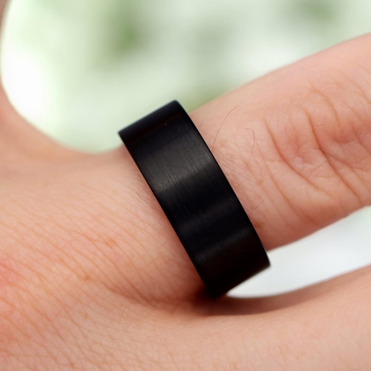 Black brushed tungsten whiskey barrel wedding band worn on a finger, seen from above