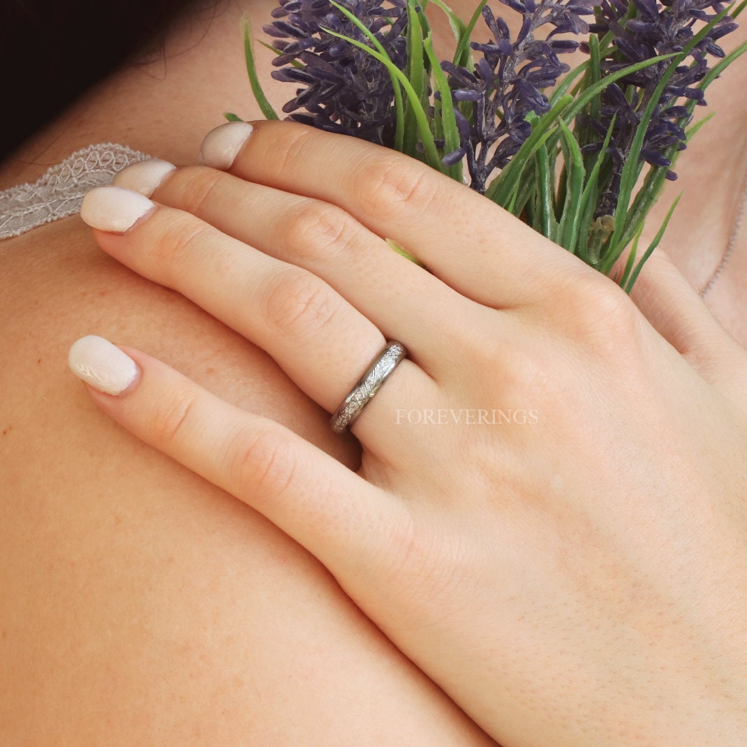 Woman wearing a 4mm silver tungsten band with meteorite-look inlay on her ring finger