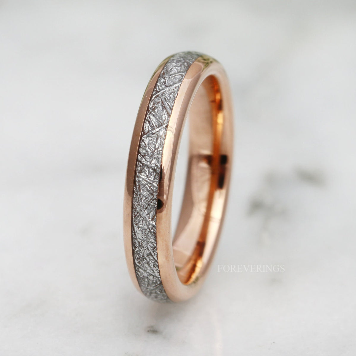 Rose gold tungsten band with meteorite-look inlay standing on edge, on white marble
