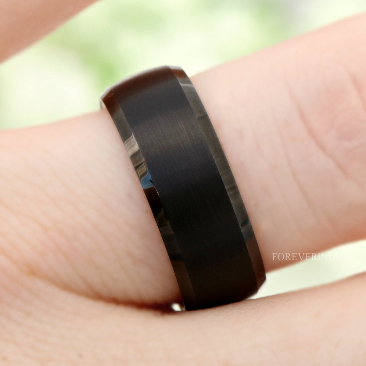 Black tungsten whiskey barrel wedding band worn on a finger, angled from above