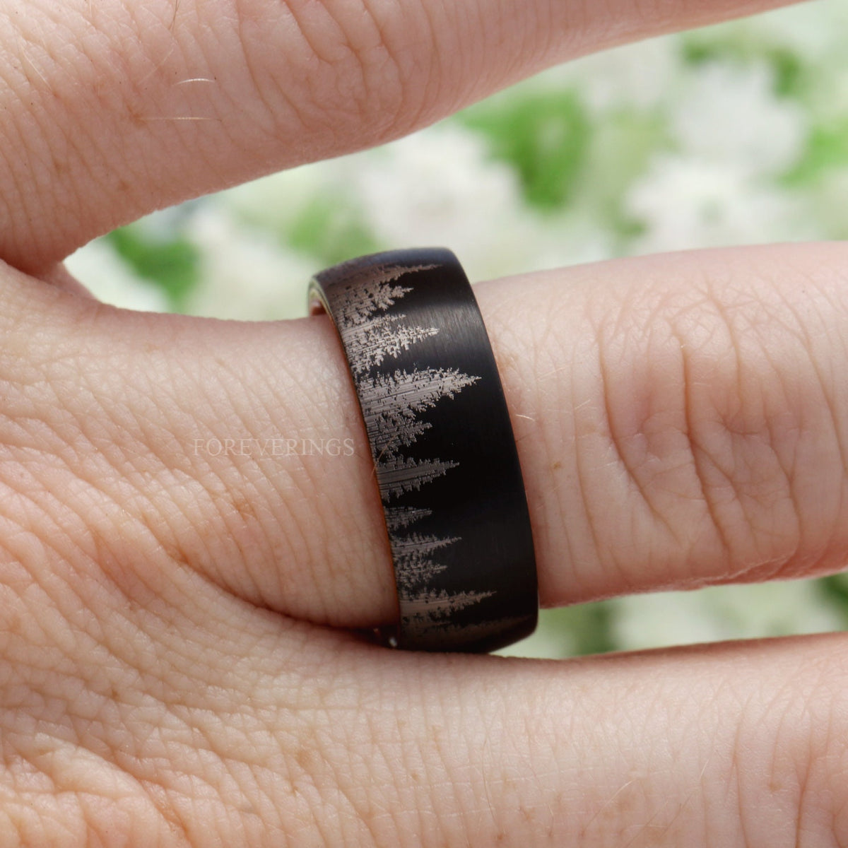 Black tungsten and whiskey barrel wood band worn on a finger, close-up