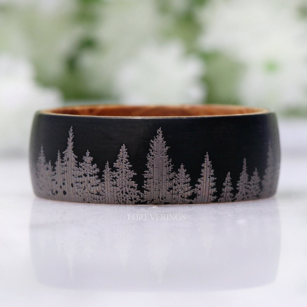 Black tungsten whiskey barrel band lying flat, forest tree-line shown straight on
