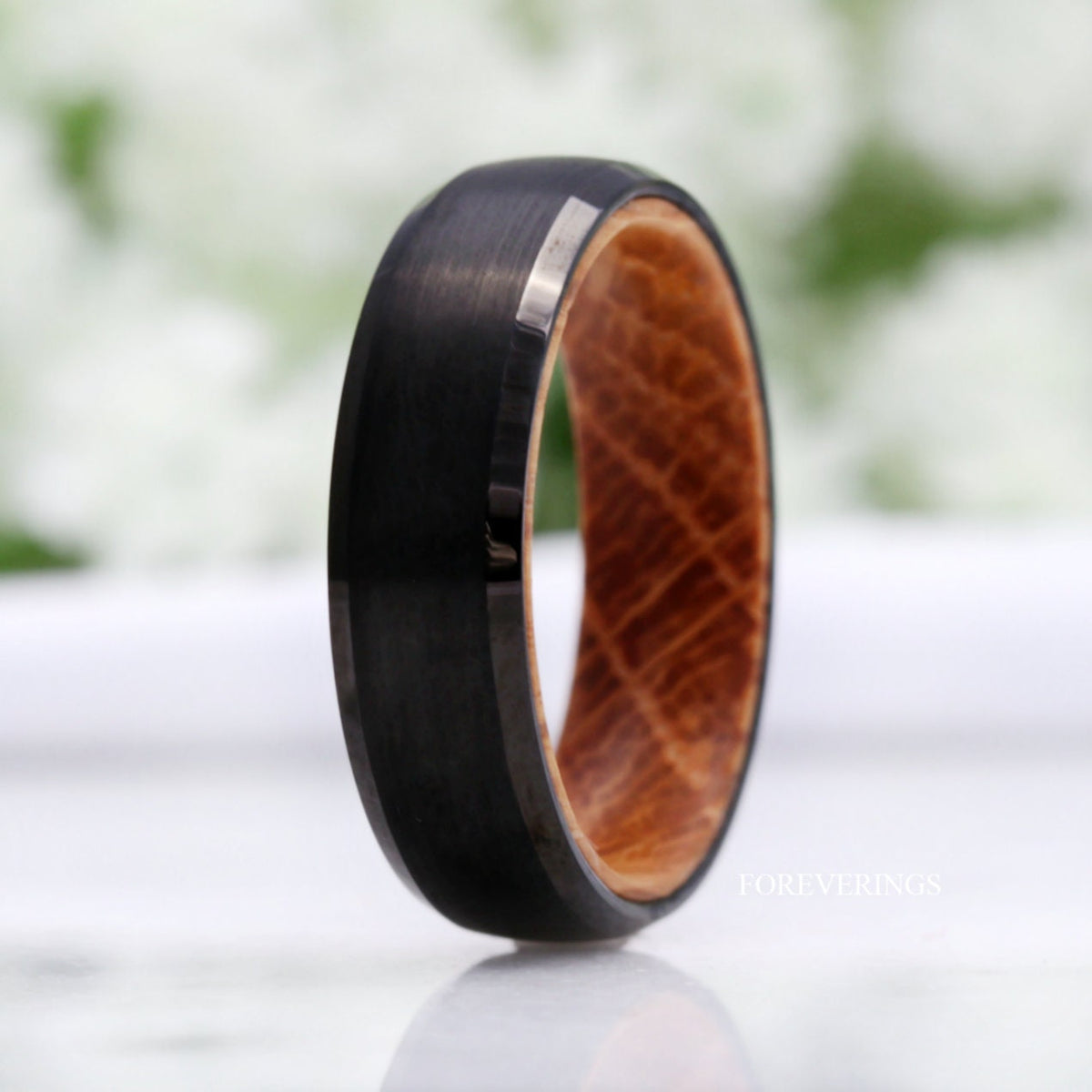 Black tungsten band standing upright, angled to show the whiskey barrel wood interior