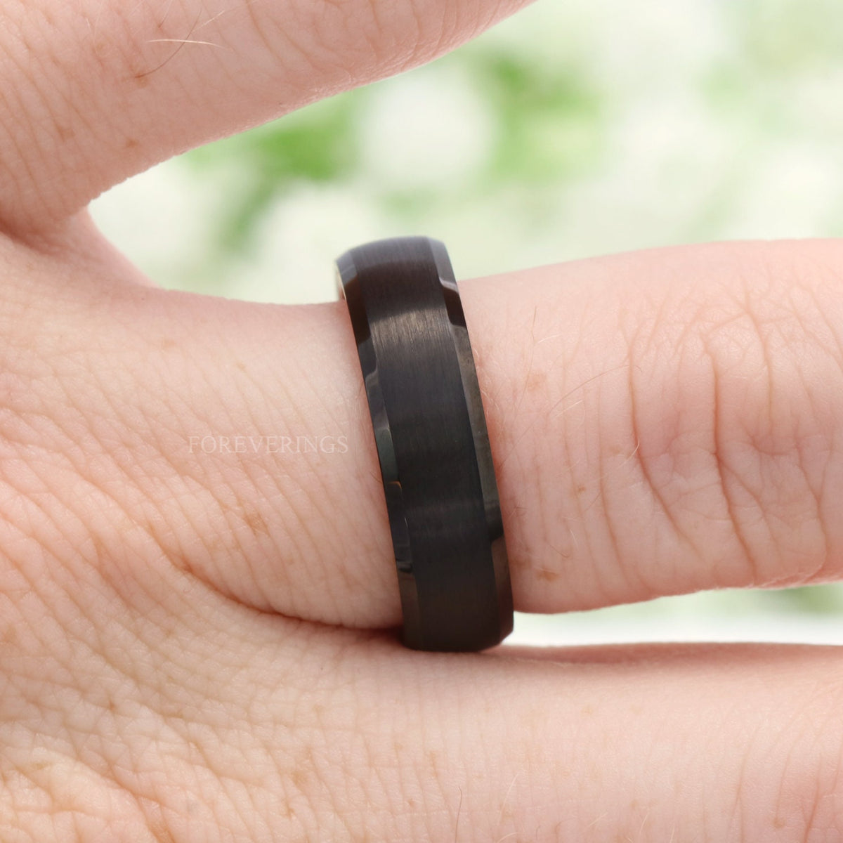Men's black whiskey barrel band on a finger, side view of the beveled edge