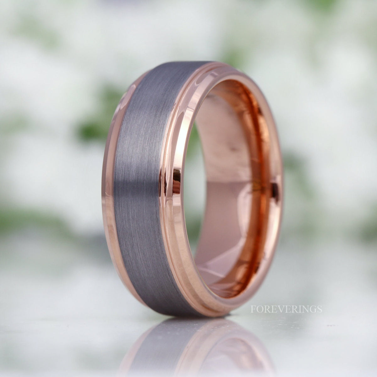 Two-tone silver and rose gold tungsten band standing upright, side view with reflection