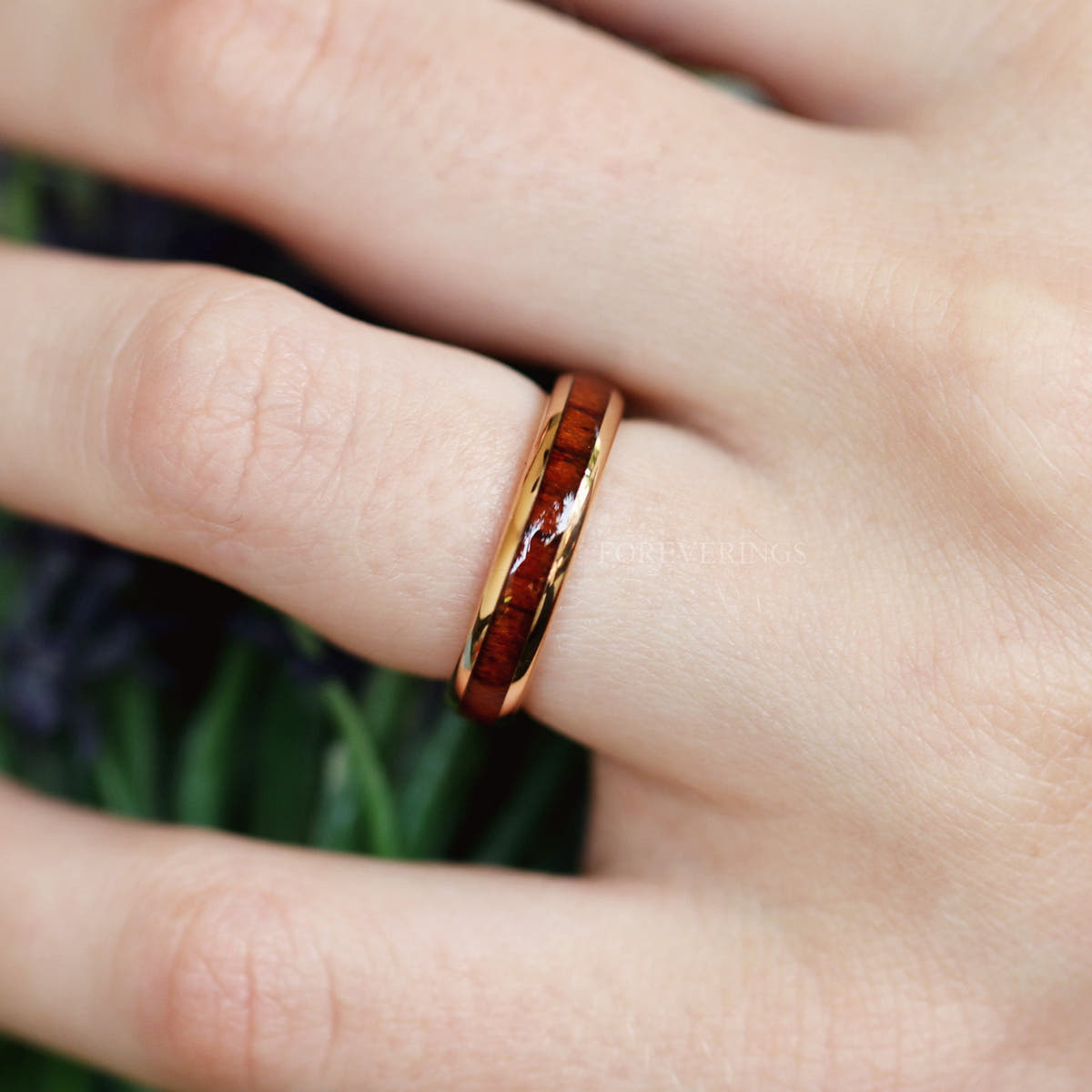 Koa wood tungsten band worn on a finger, angled from above
