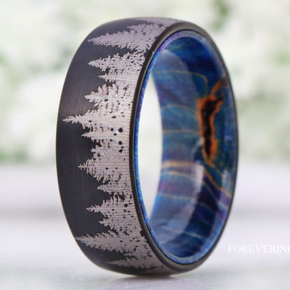 Men's brushed black tungsten band with etched pine tree line and blue elder wood lining, close-up
