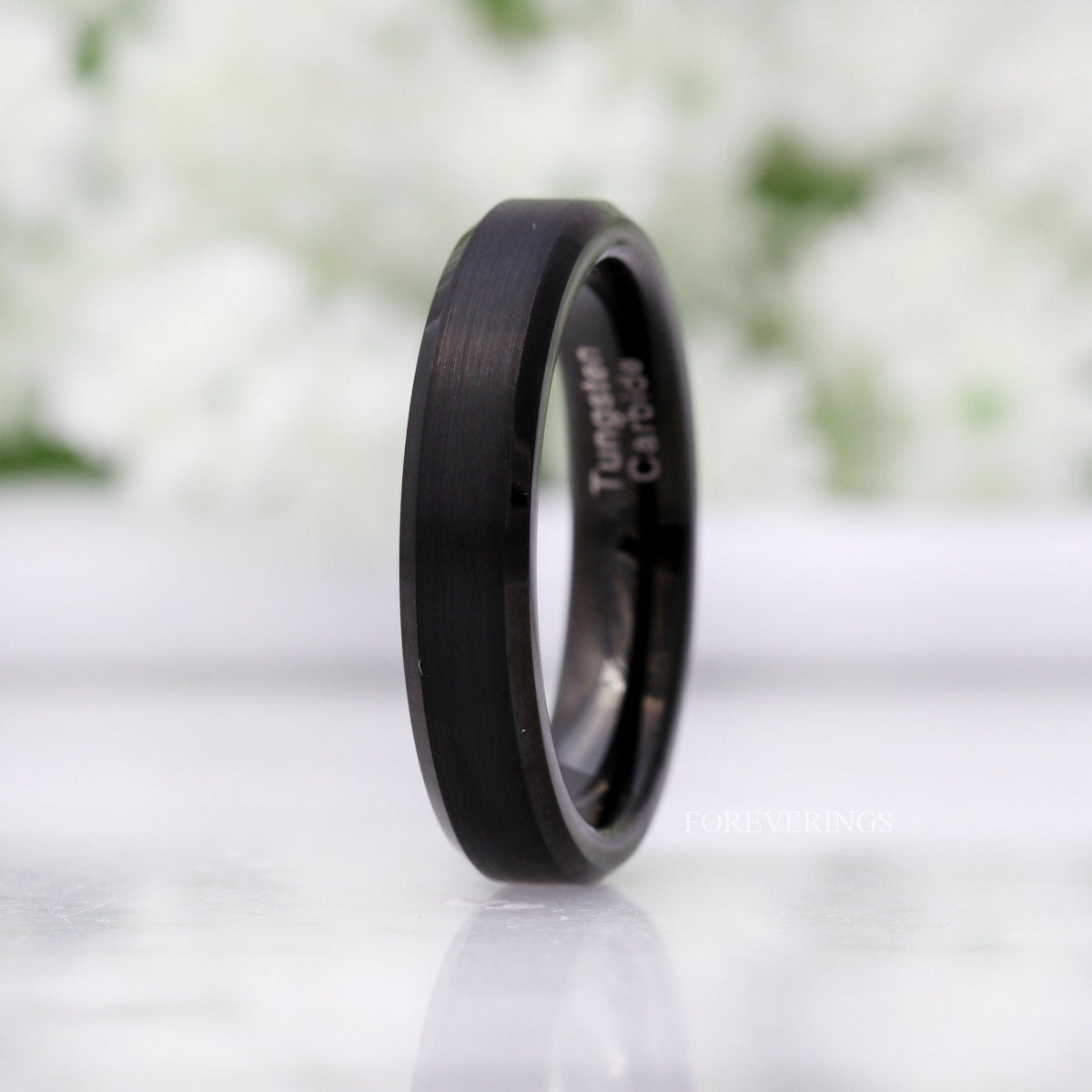 Women's 4mm matte black tungsten band with beveled edges, standing at an angle