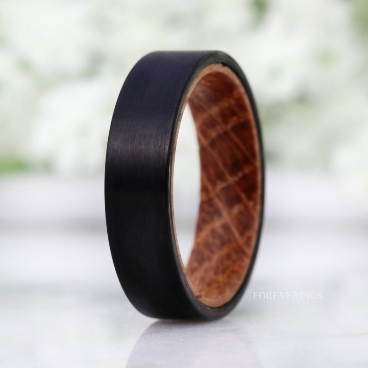 Men's 6mm black brushed tungsten band lined with whiskey barrel wood, standing on edge
