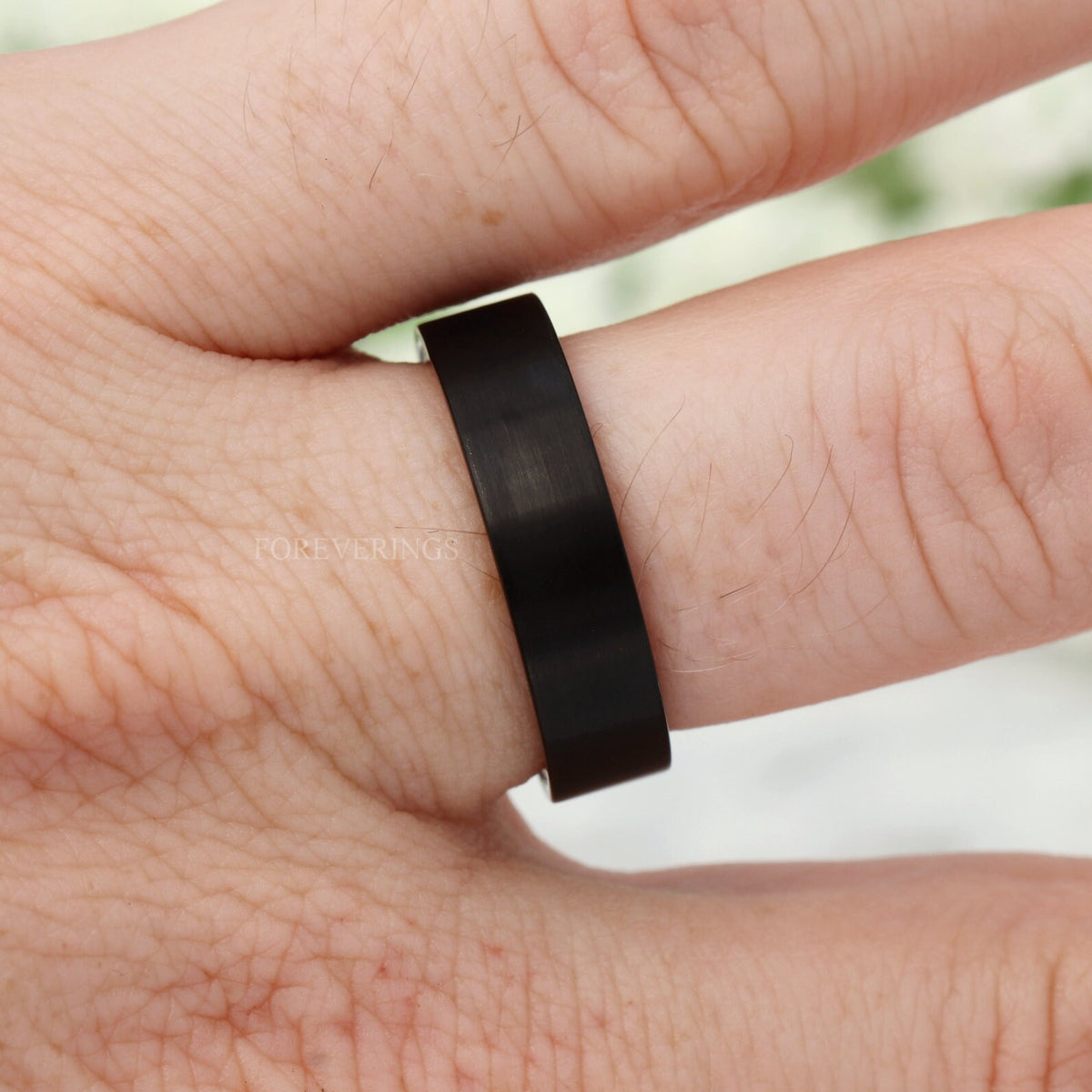 Black brushed tungsten whiskey barrel wedding band worn on a hand, front view