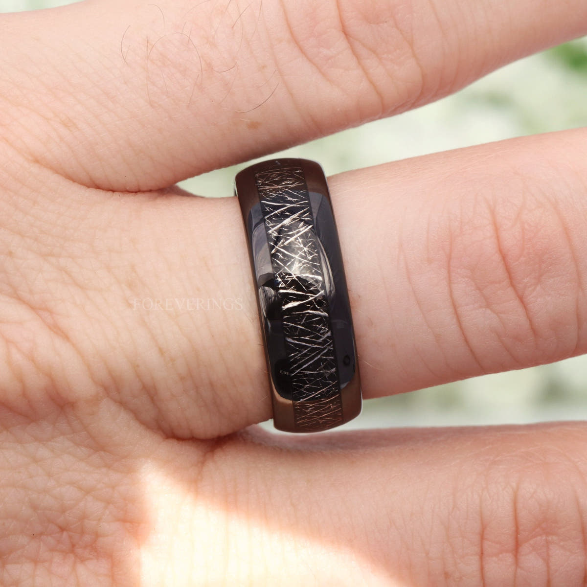 Black tungsten band with meteorite-look inlay worn on a finger, close-up