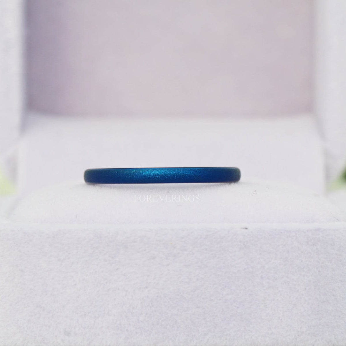 Thin blue sandblasted tungsten band resting in a white ring box