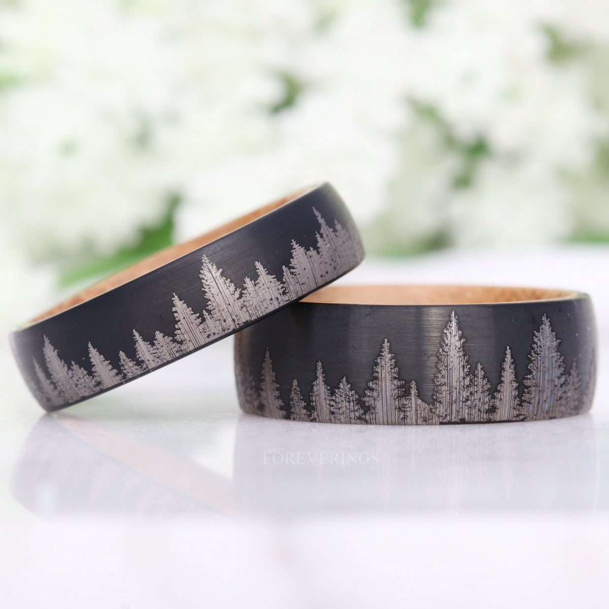 Two widths of the black tungsten pine tree band with whiskey barrel wood, one leaning on the other