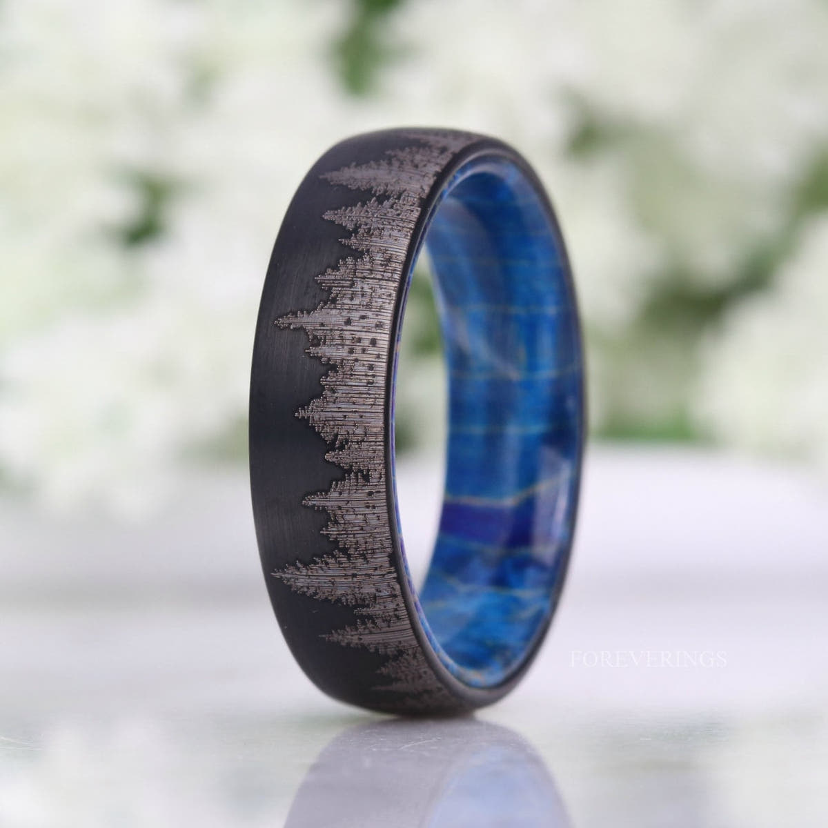 Brushed black tungsten band with pine forest etching, narrow side view of the blue wood