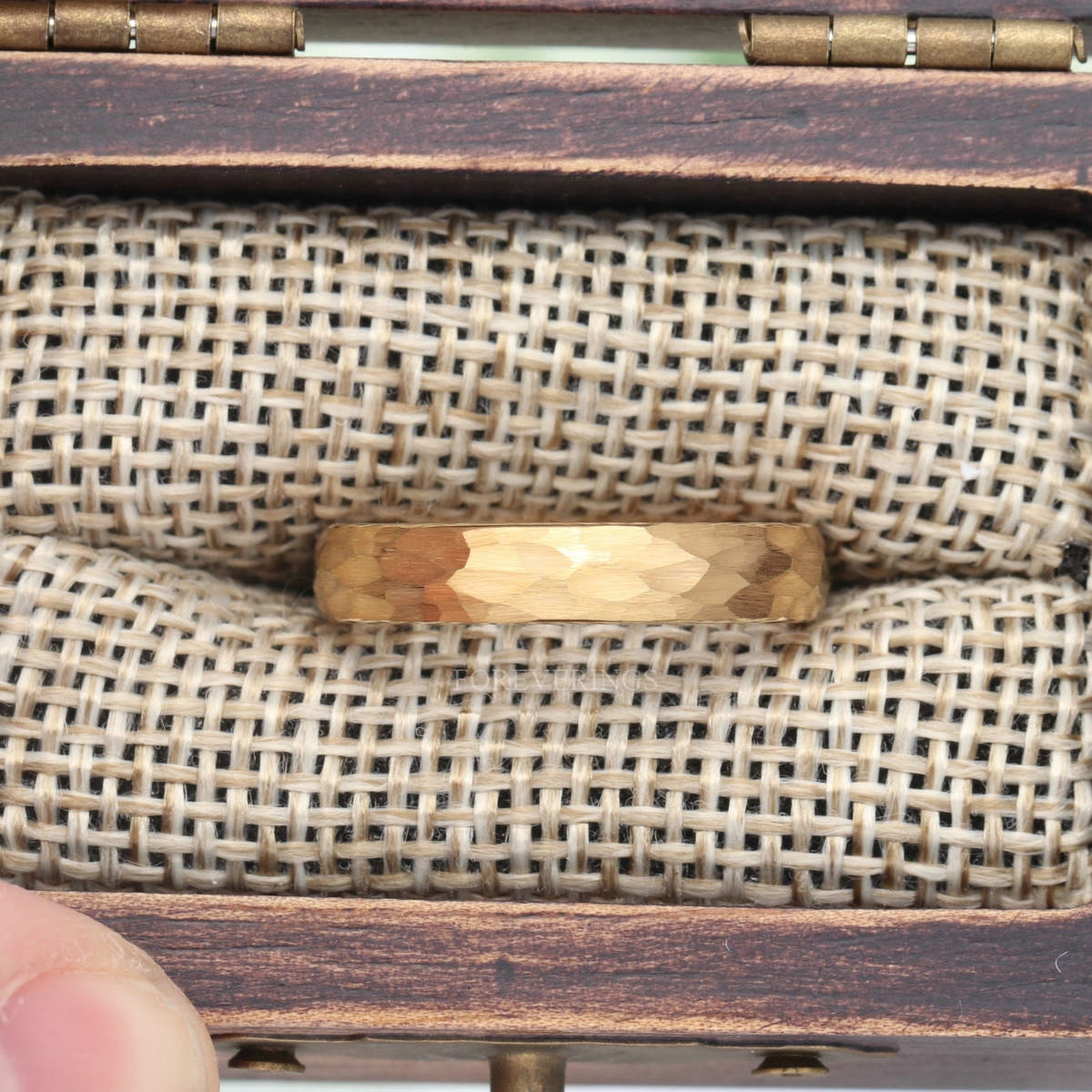 Wider 4mm hammered gold tungsten band nestled in the burlap insert of a rustic wood ring box