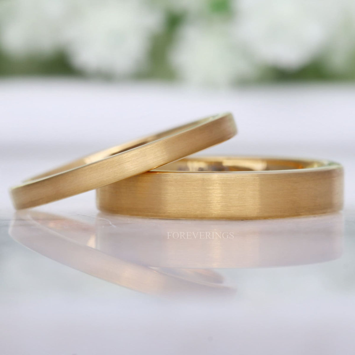 Matte gold tungsten wedding bands in 2mm and 4mm, flat profile, leaning together