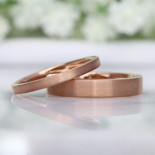 Matte rose gold tungsten flat bands in 2mm and 4mm, the thin band leaning on the wider one