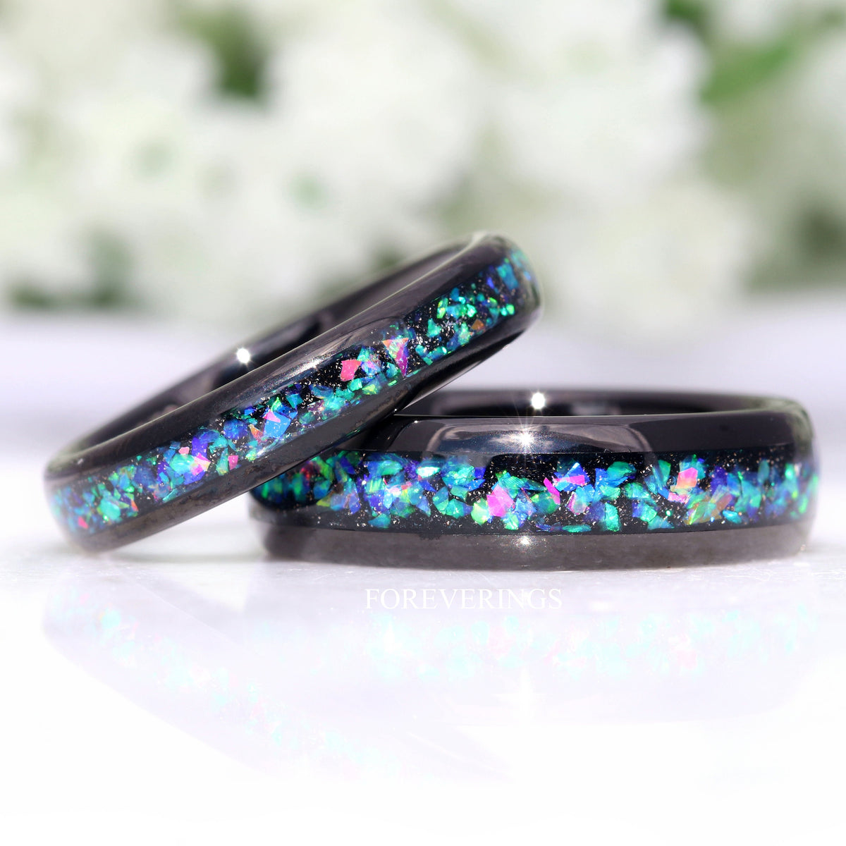 His and hers black tungsten wedding bands with galaxy opal inlay, her 4mm ring leaning on his 6mm