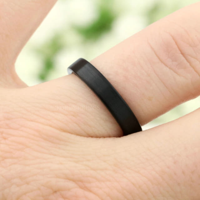 4mm matte black tungsten flat band worn on a finger, angled view