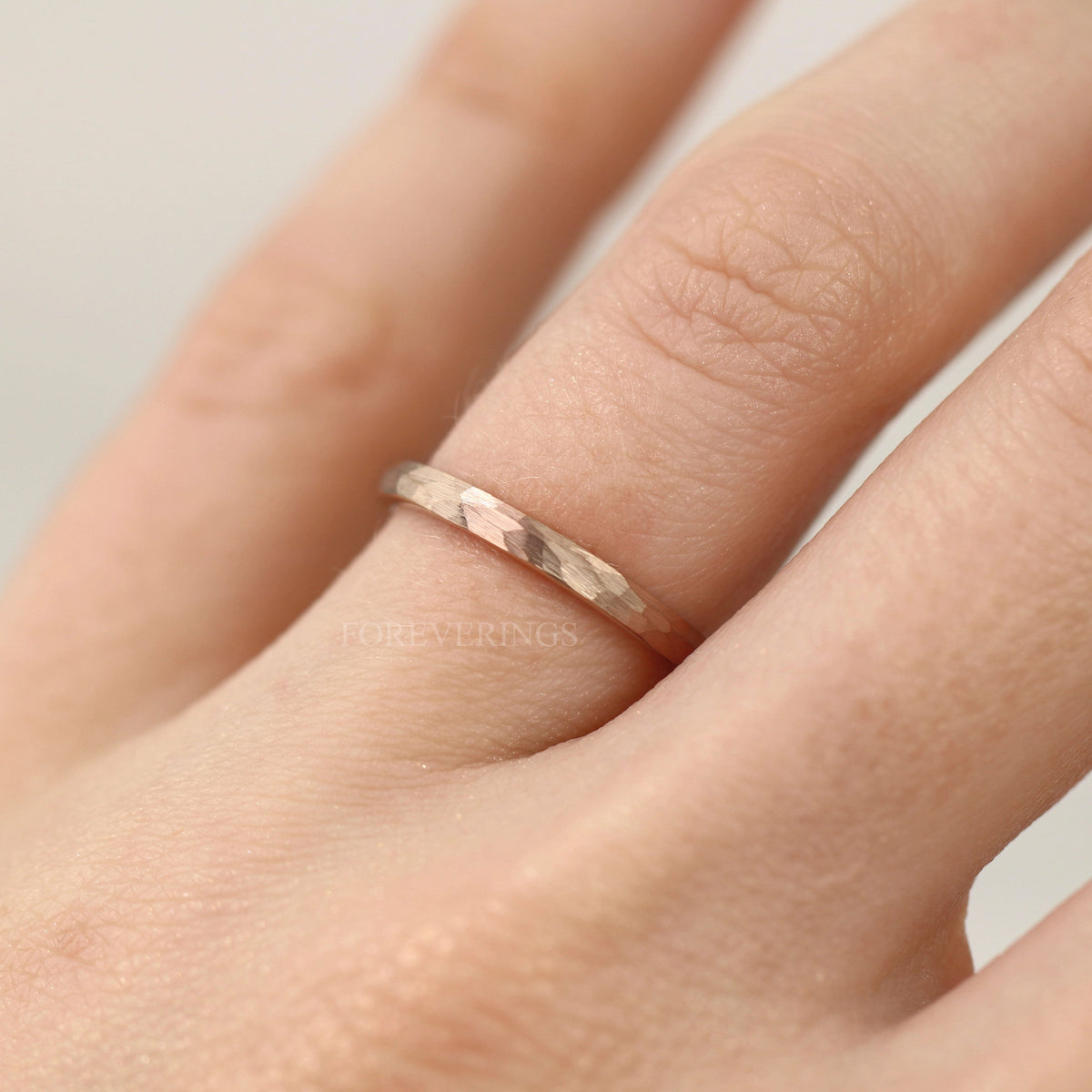 2mm hammered rose gold tungsten band worn on a finger, close view