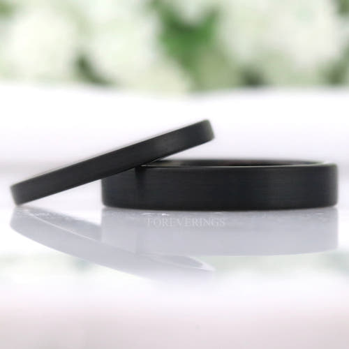 Thin matte black tungsten wedding bands in 2mm and 4mm, flat profile, leaning together