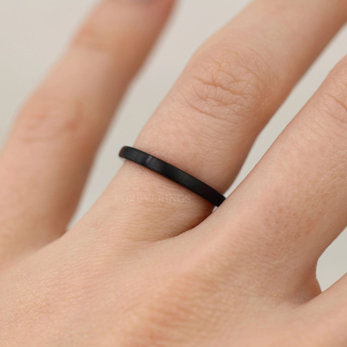 Thin matte black tungsten band worn on a woman's finger