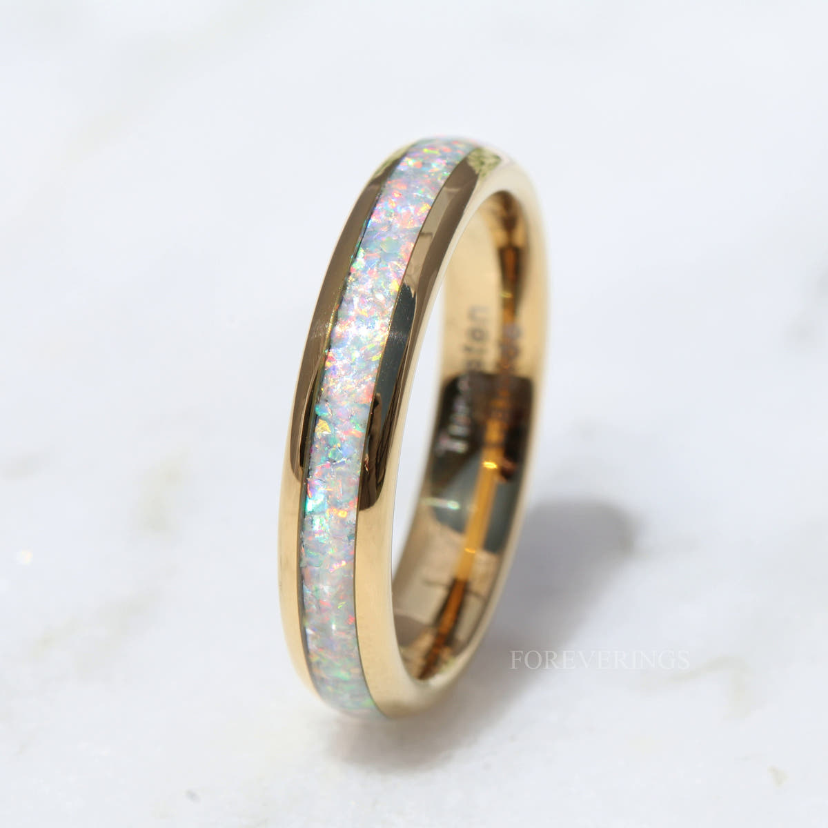 Polished dome gold tungsten band with white opal inlay leaning at an angle, close view