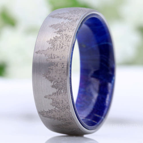 Men's brushed silver tungsten band with a pine forest engraving and blue elder wood lining, standing upright