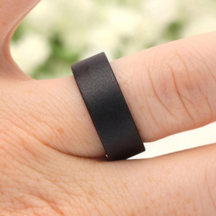 Black tungsten whiskey barrel wood band worn on a finger, flat sandblasted top