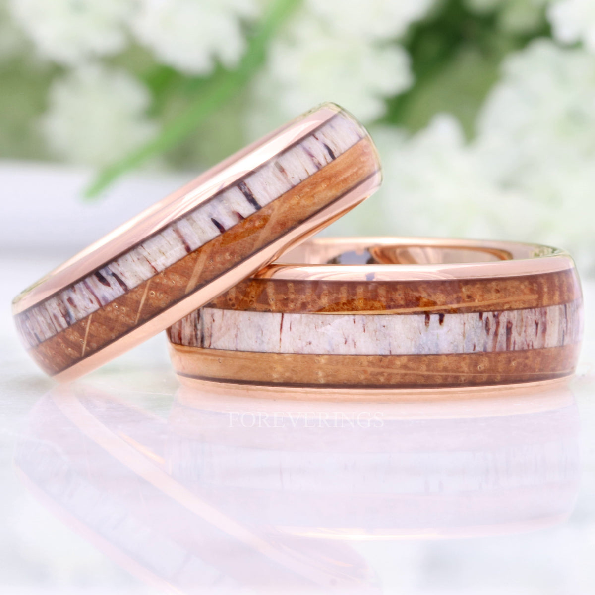 Men's rose gold tungsten bands with whiskey barrel wood and antler inlay, a narrower band leaning on a wider one